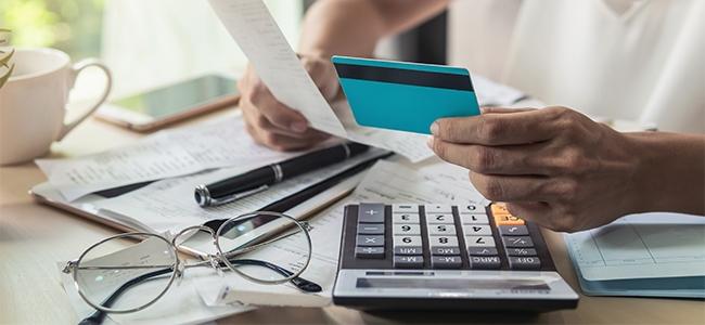 A man sits at a table with calculator and financial documents, holding credit card