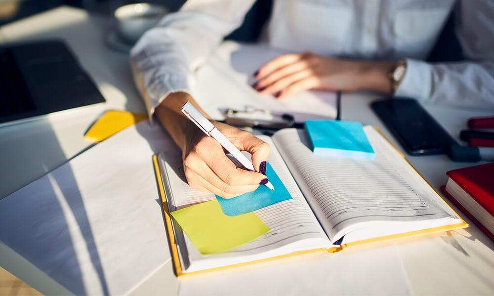 a woman writes down notes in notebook to plan for future