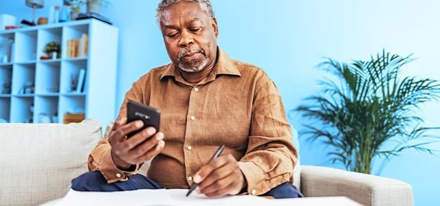 A man sits looking at mobile phone and writing