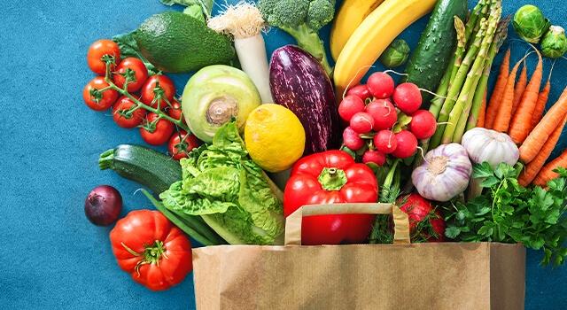 A grocery bag overflows with fruits and vegetables