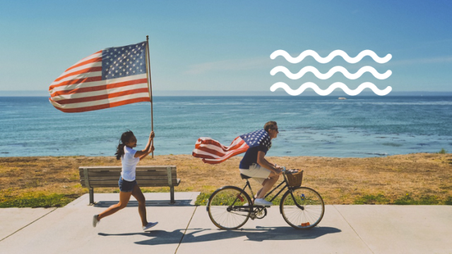 Girl runs with U.S. flag while friend rides bike along shoreline